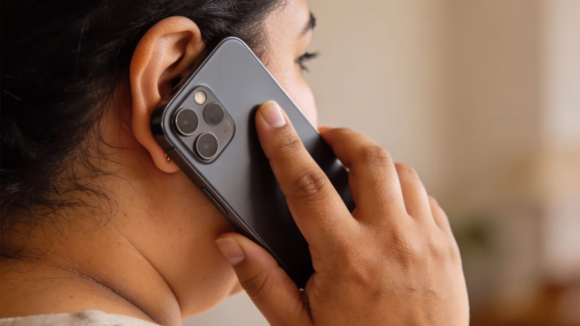 Persona sosteniendo un teléfono móvil negro con triple cámara junto a su oído.