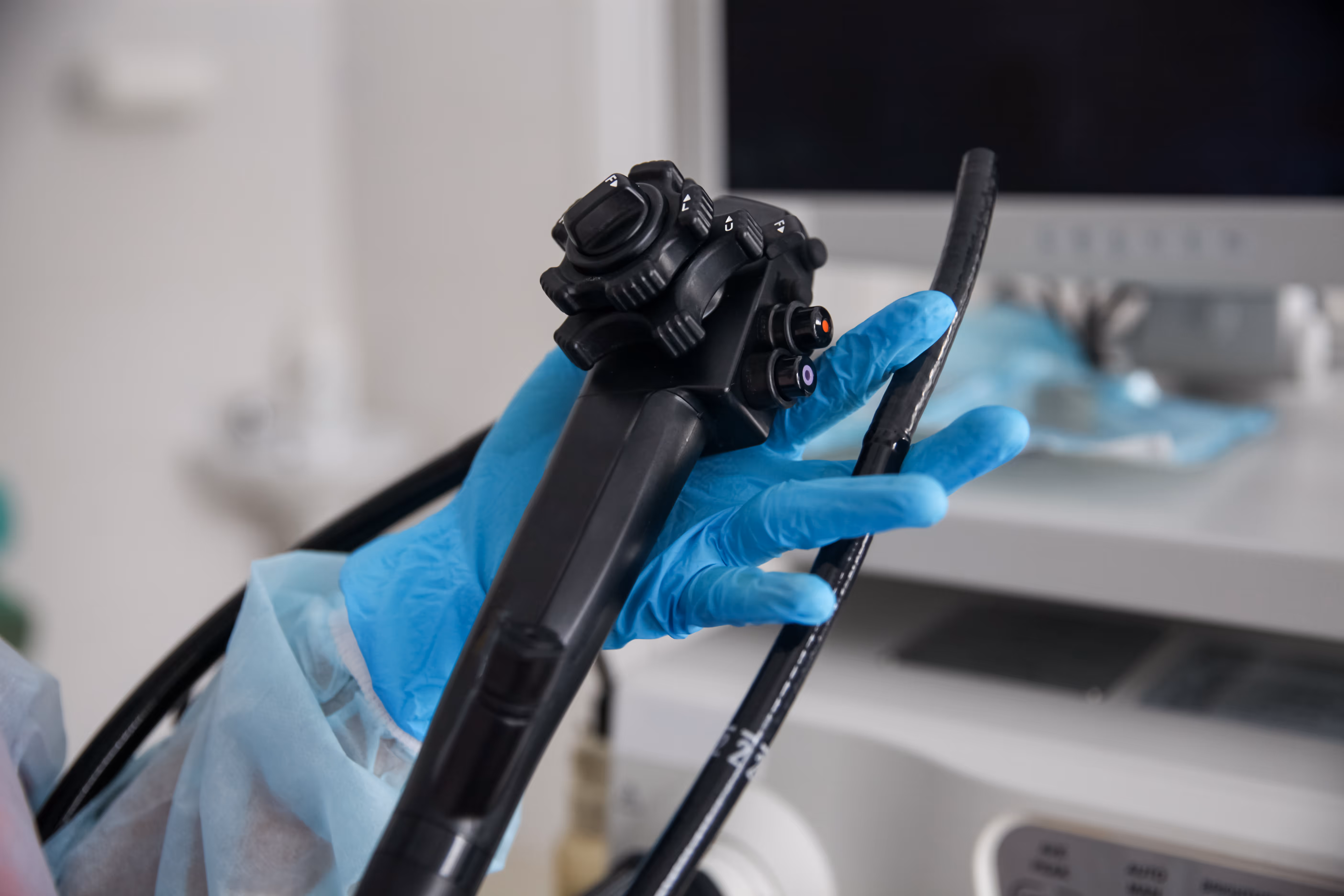 Mano con guante azul sosteniendo un endoscopio negro en un entorno médico.